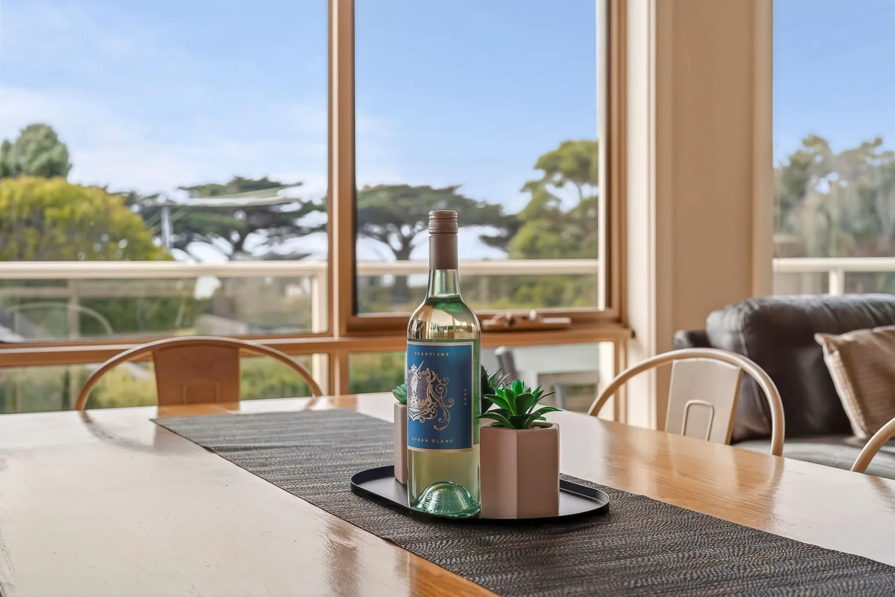 Una mesa de comedor con una botella y una planta está junto a grandes ventanas.