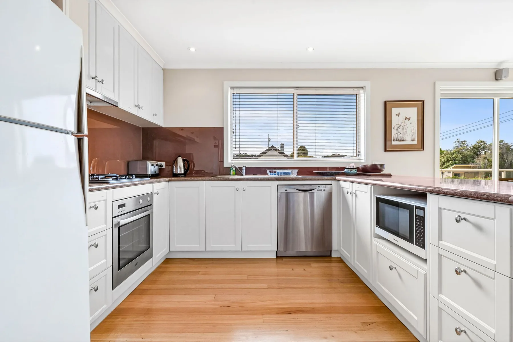 Una cocina luminosa con gabinetes blancos, electrodomésticos de acero inoxidable y piso de madera.