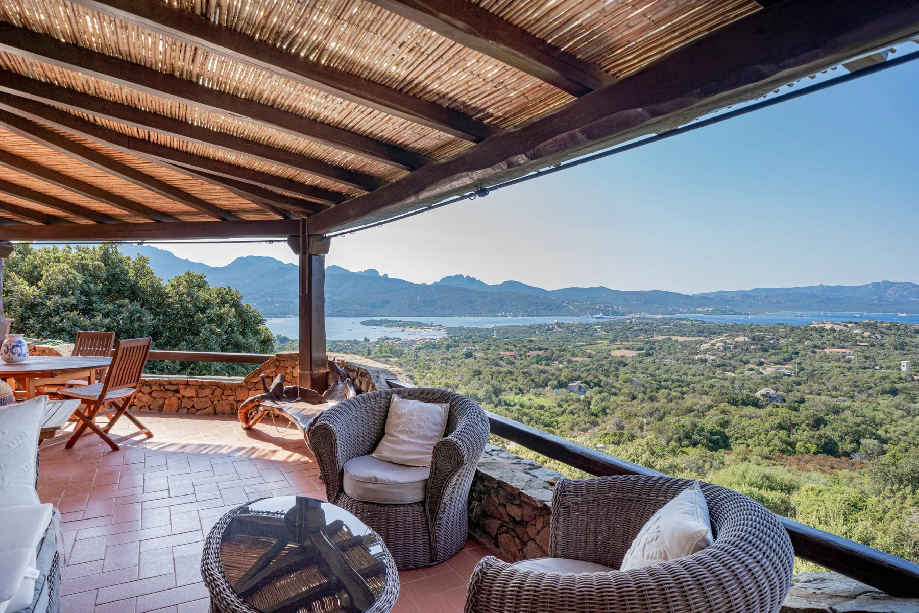 A covered outdoor terrace with seating overlooks a green landscape and distant water.