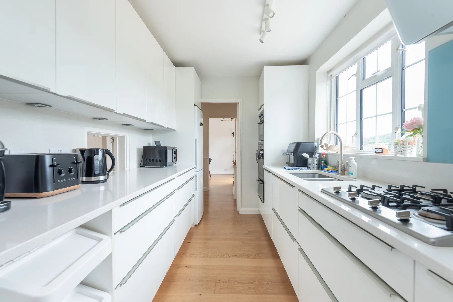 Cocina luminosa con armarios blancos, encimeras y una ventana grande.