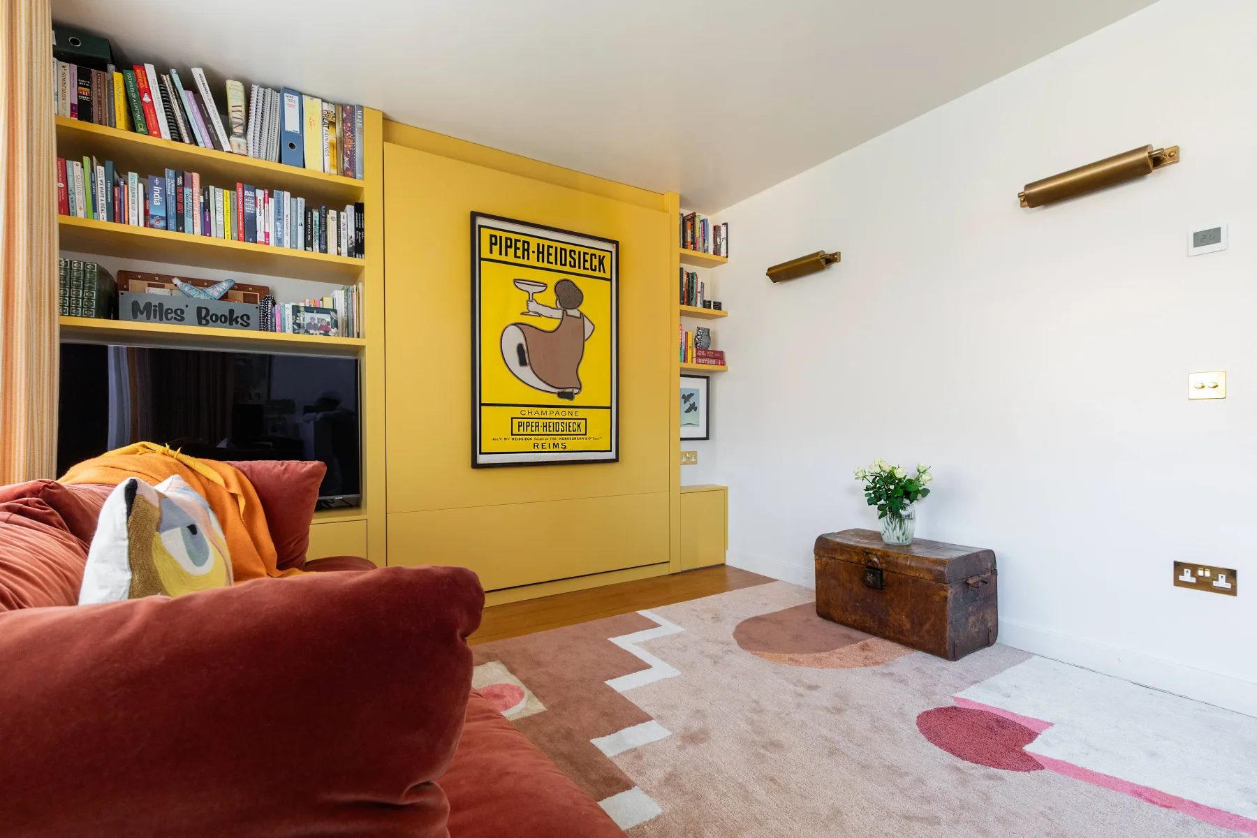 A colorful living room with built-in bookshelves and a patterned rug.