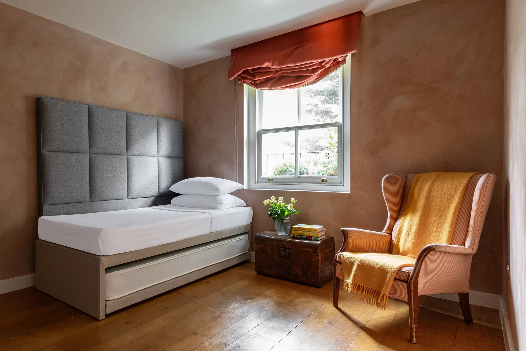 A bedroom with a single bed, a window, and an upholstered armchair.
