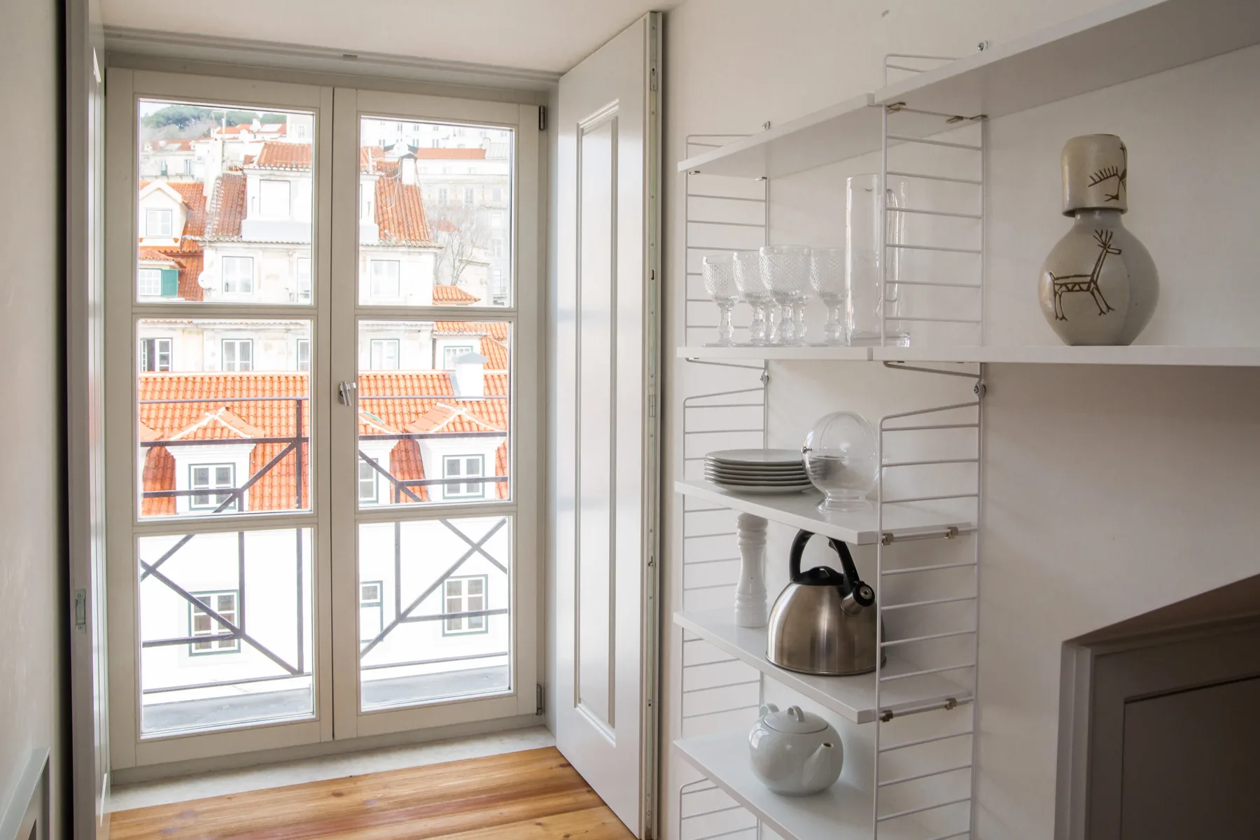 A bright room with a tall window and open shelving beside it.