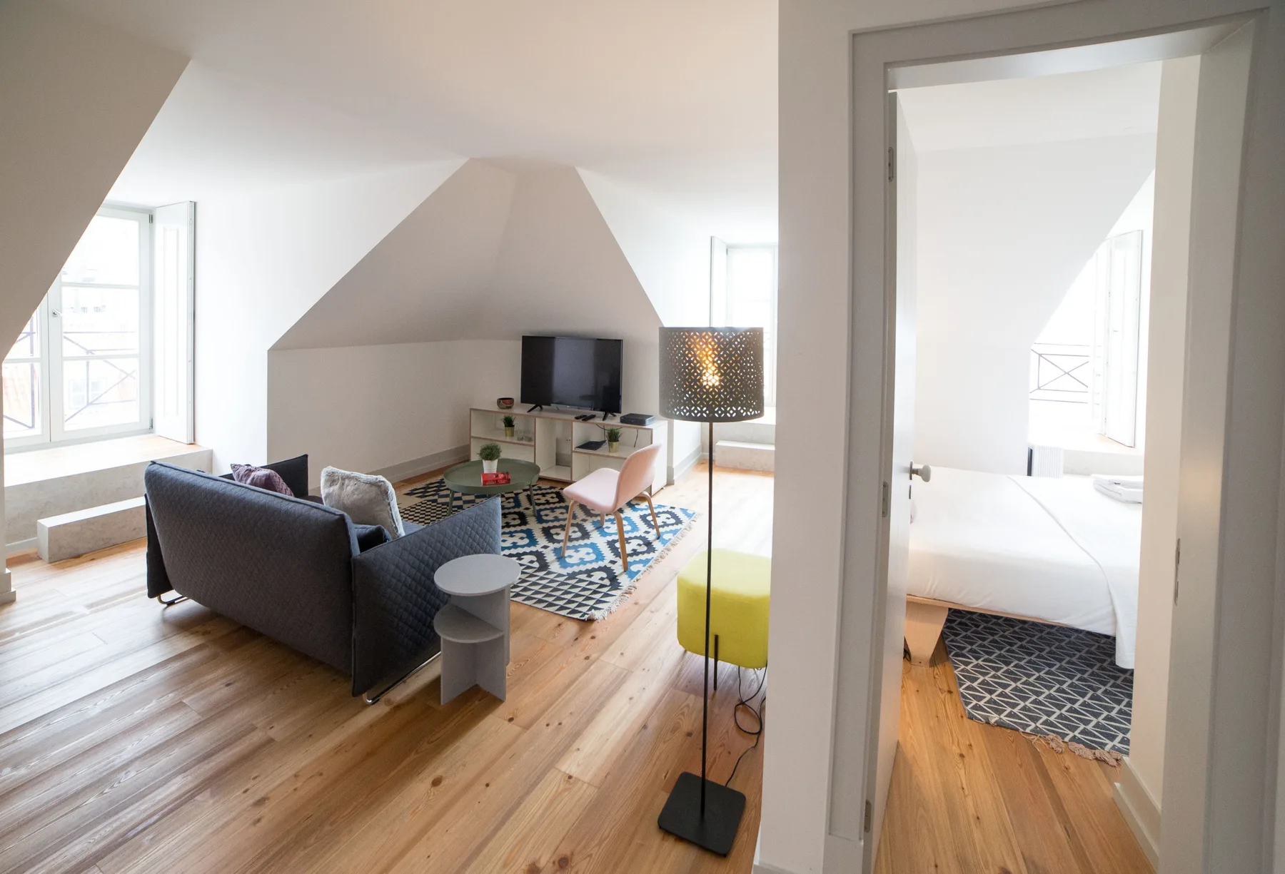 A bright living room with seating, a television, and an open doorway to a bedroom.