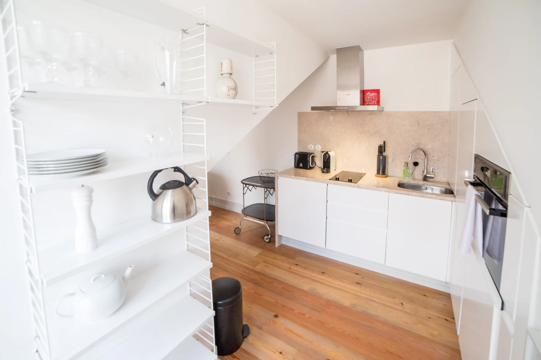 A bright kitchen with open shelves, a countertop, and wooden flooring.