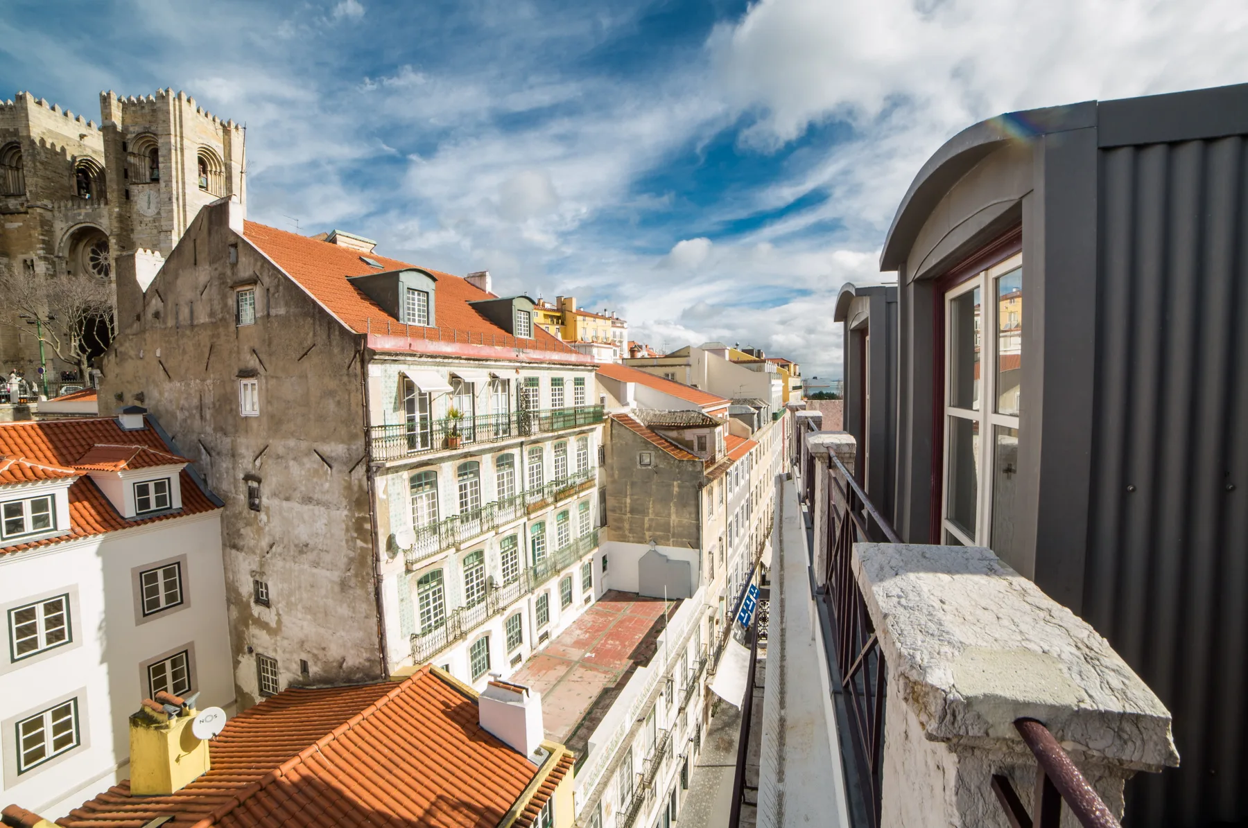 View from a balcony over city rooftops and historic buildings beneath a partly cloudy sky.