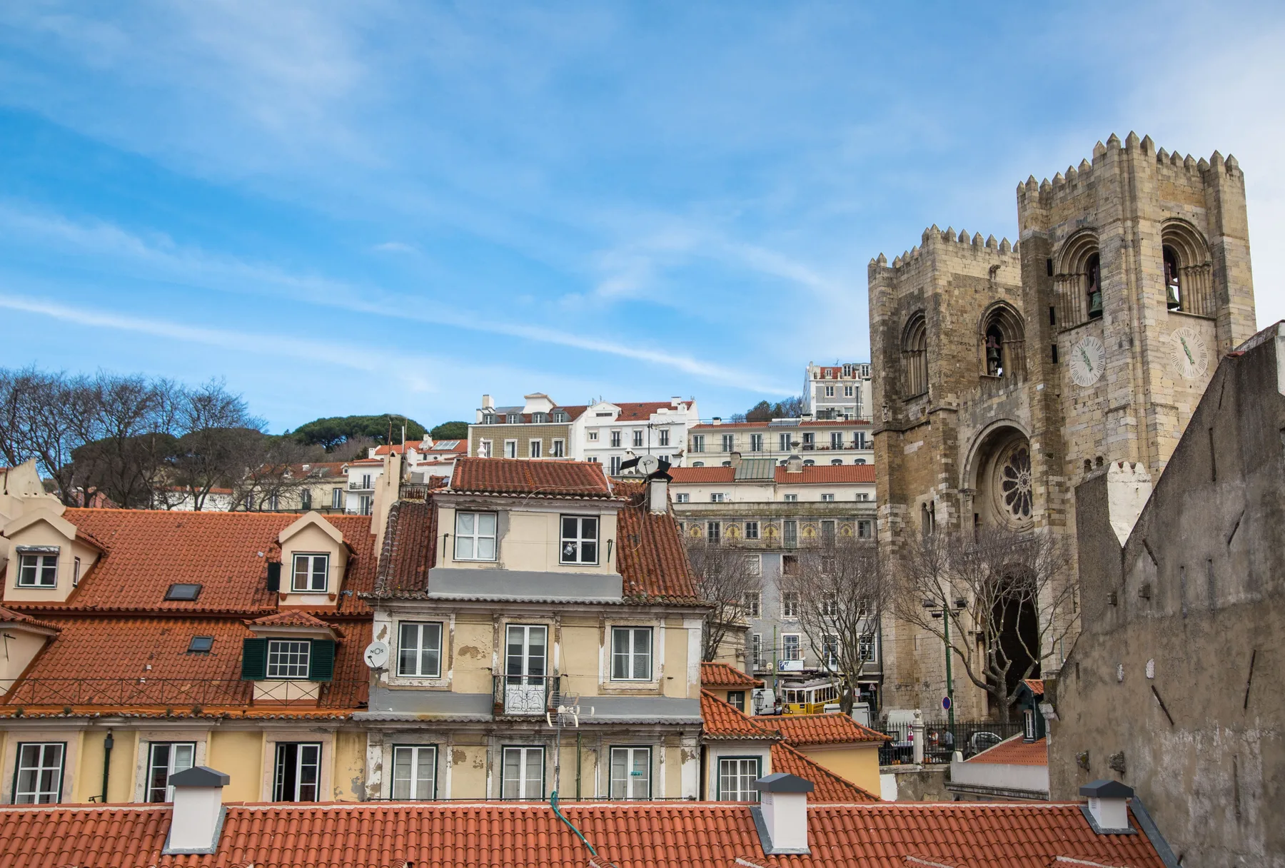 Historic stone church towers rise above red-tiled rooftops under a blue sky.