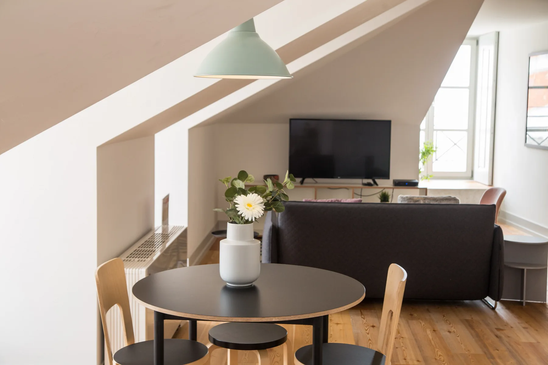 A bright attic living area with a dining table and seating facing a television.