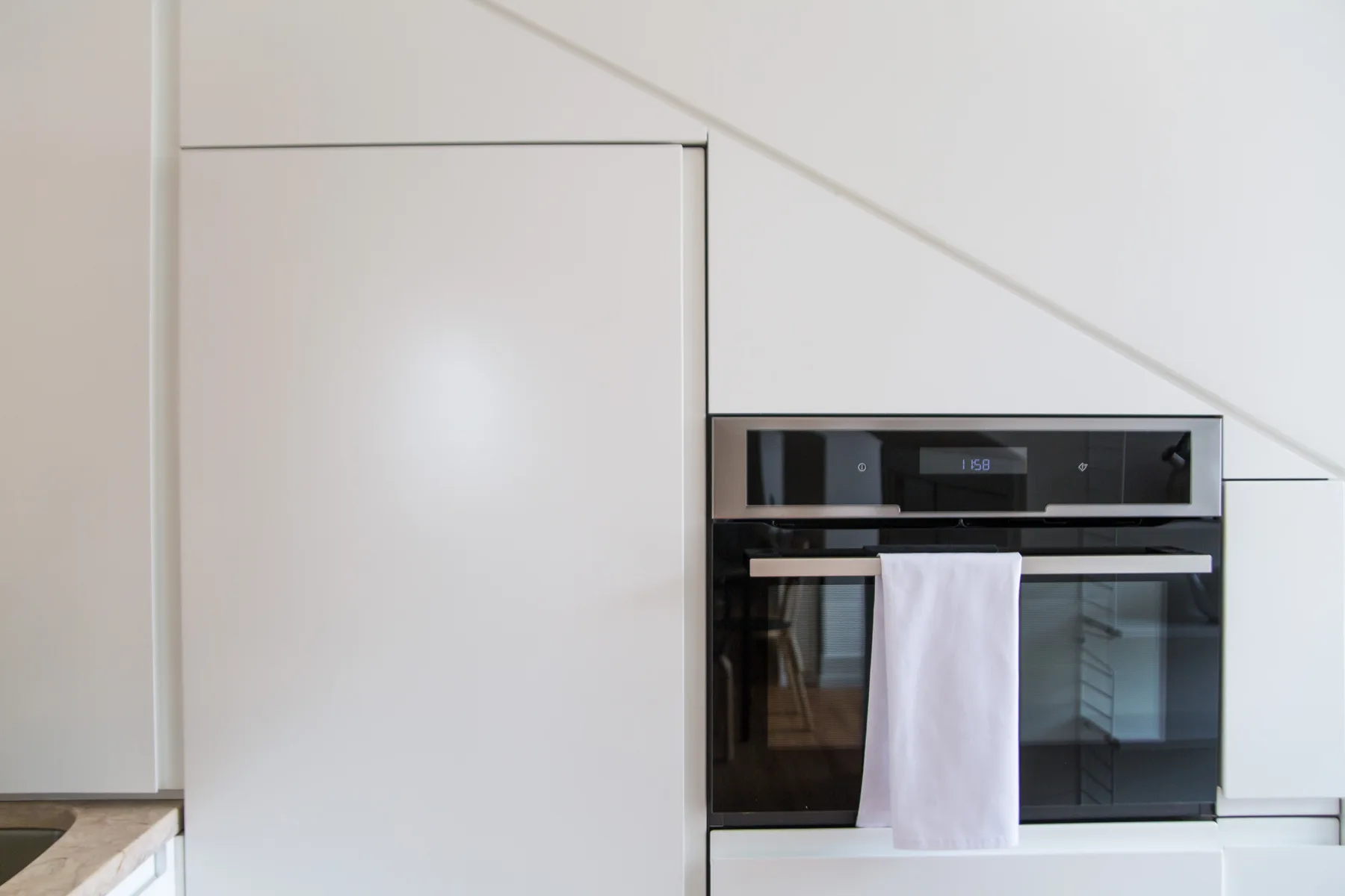 A modern kitchen with a built-in oven and a white towel hanging from the handle.