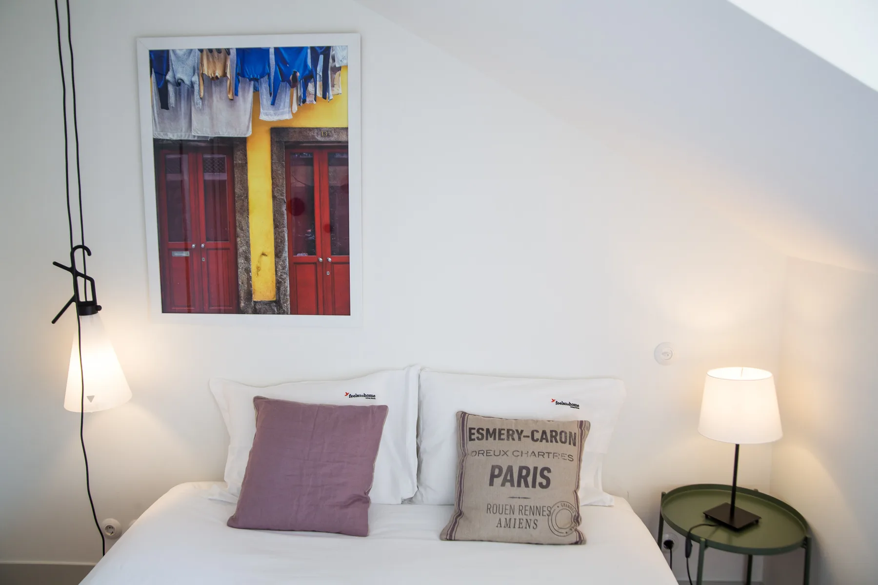 A bedroom with a bed, framed artwork, and bedside lamps.