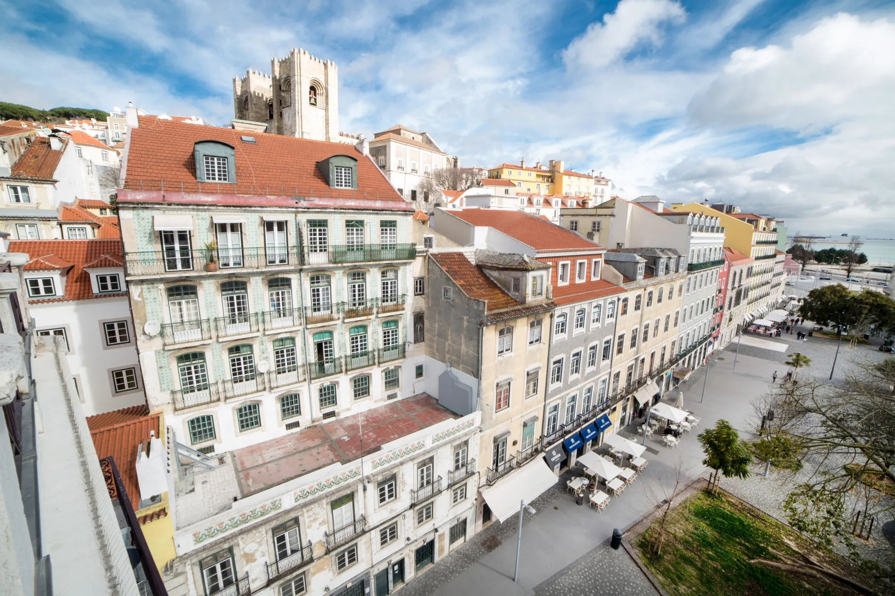 A cityscape of historic buildings with red-tiled roofs along a broad pedestrian plaza.