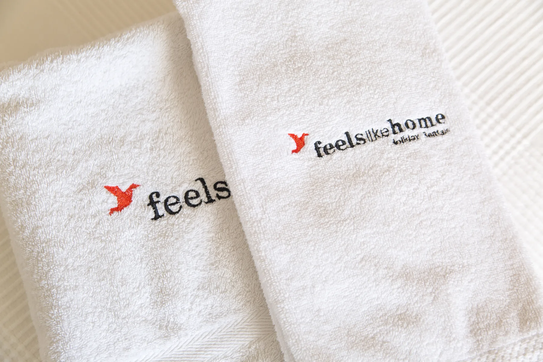 White towels with embroidered logos are arranged on a light surface.