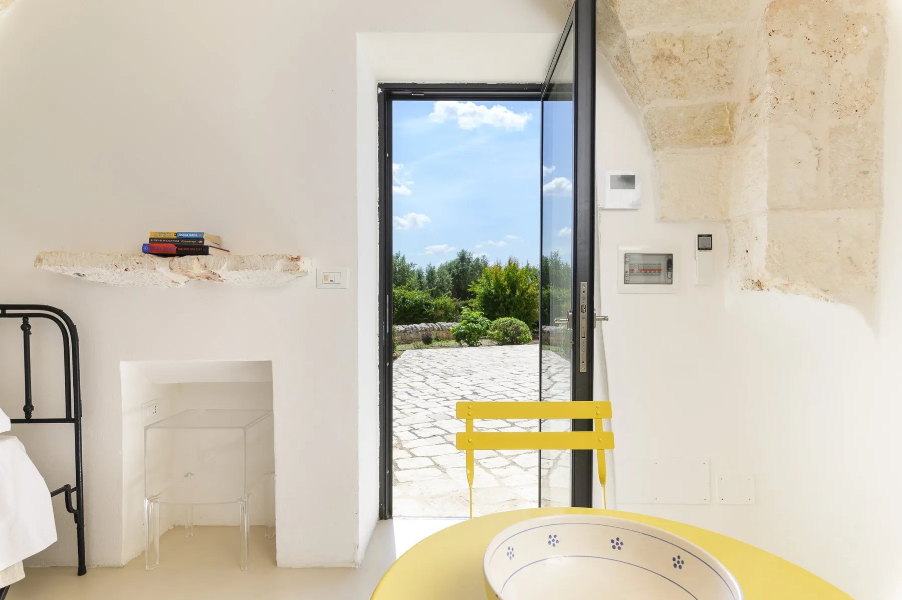 Una habitación luminosa da a un patio empedrado, con una mesa amarilla en primer plano.