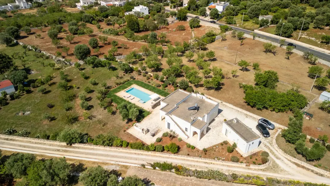 Vista aérea de una casa blanca y una piscina entre terrenos secos y cultivados.