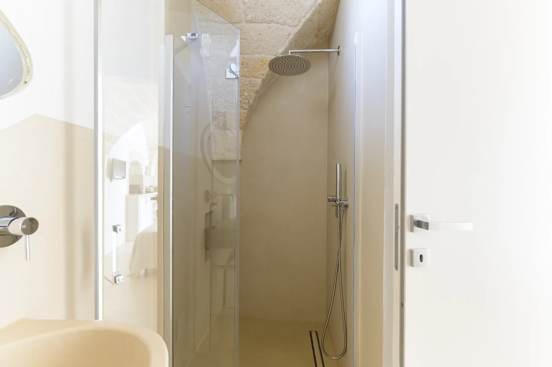 Zona de ducha en un baño, con una mampara de vidrio y un rociador en la pared.