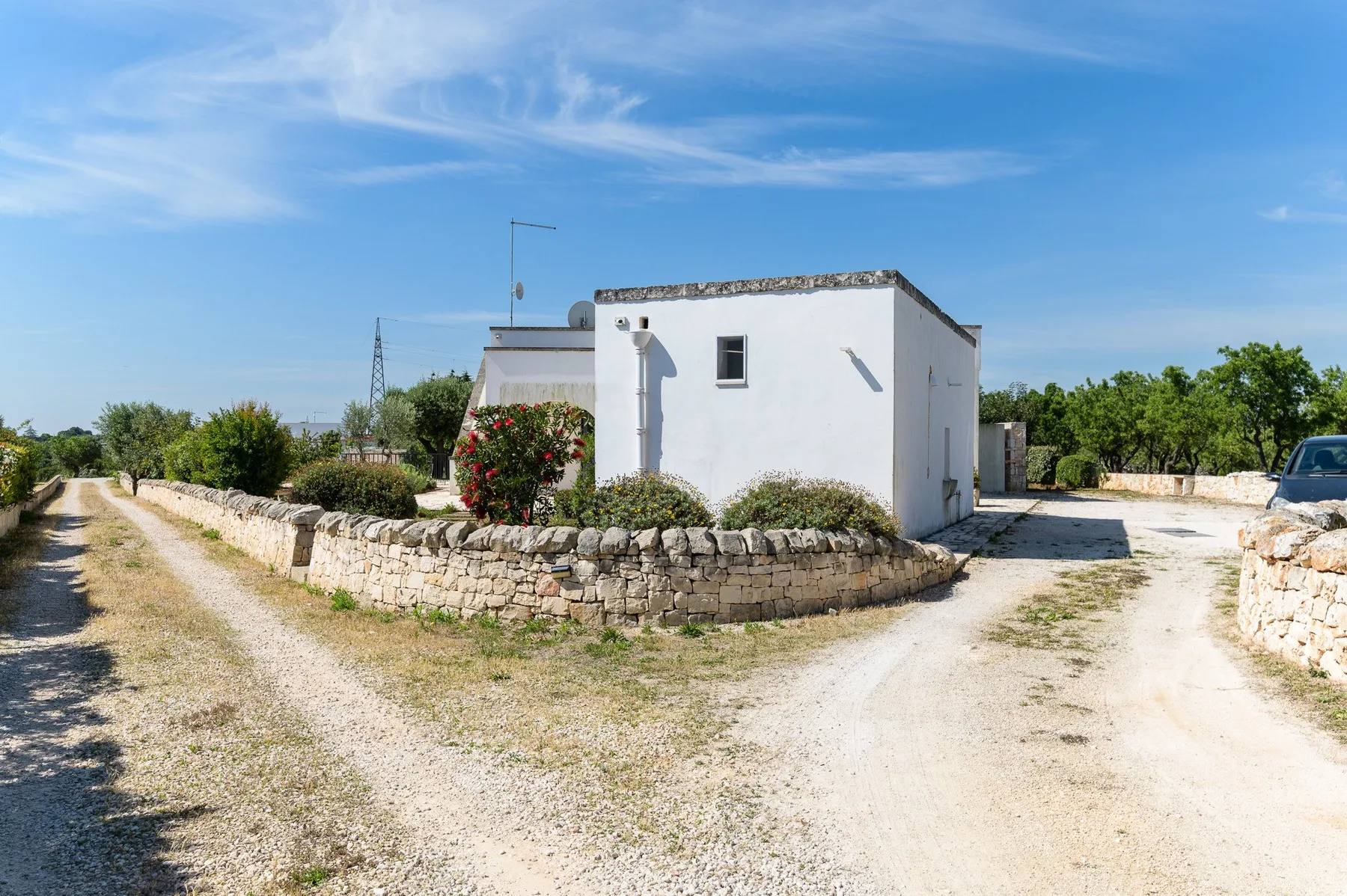 Una casa blanca se encuentra junto a un camino de grava y un muro bajo de piedra.