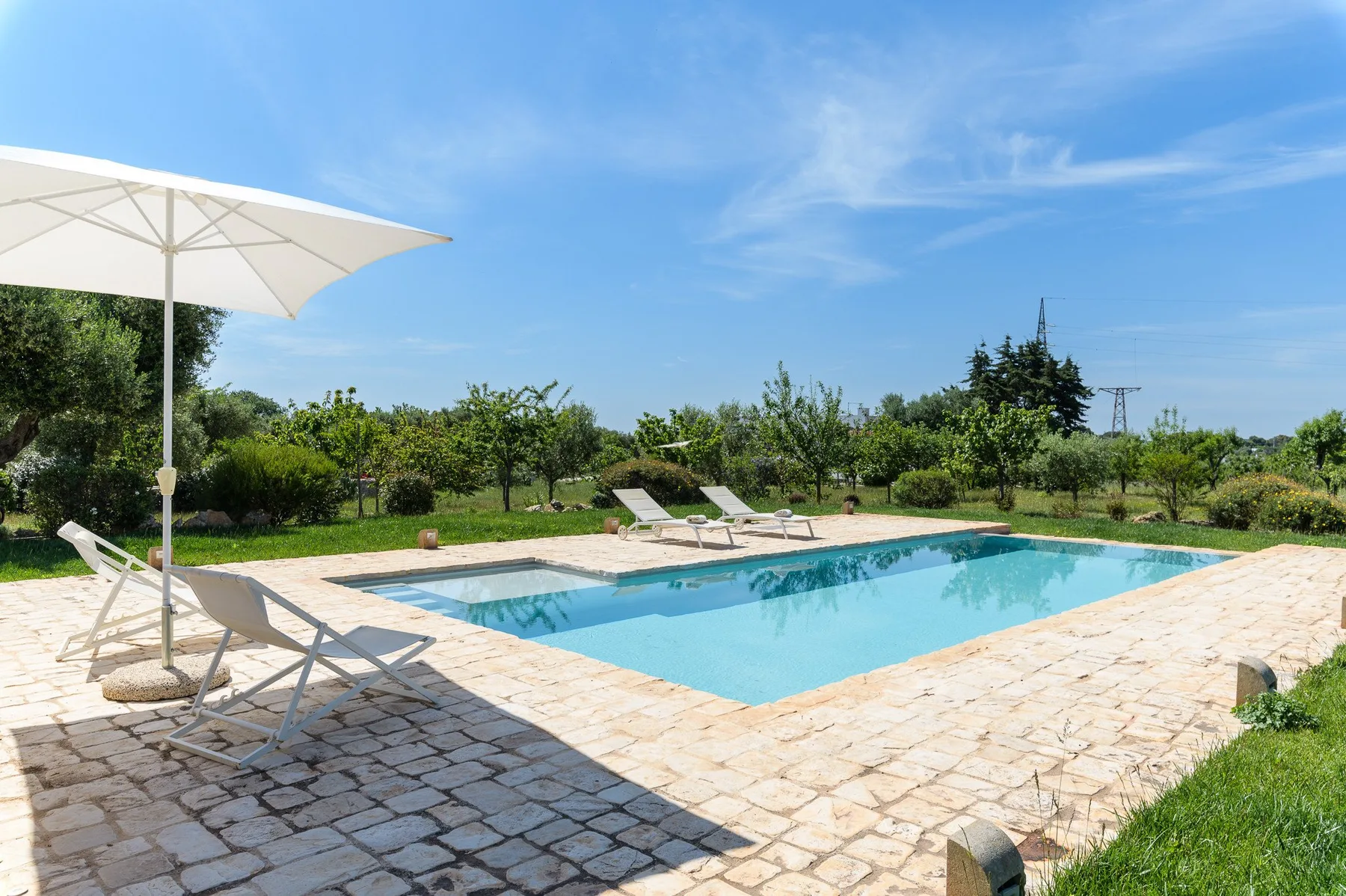Una piscina al aire libre está rodeada de una terraza pavimentada y vegetación.