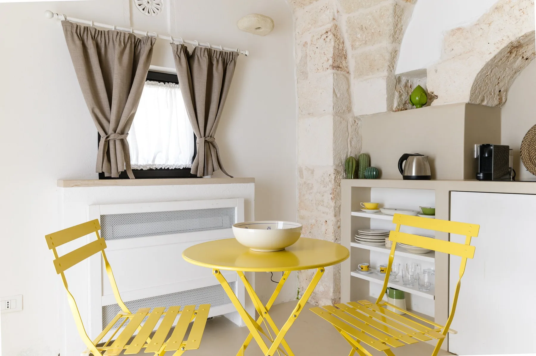 Un comedor luminoso con una mesa amarilla y sillas junto a una ventana con cortinas.