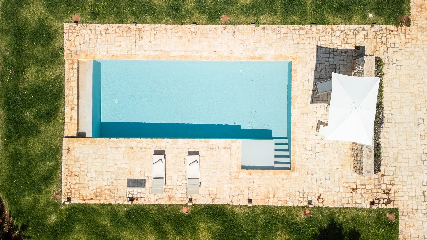 Una vista aérea muestra una piscina rectangular rodeada por un patio de piedra.