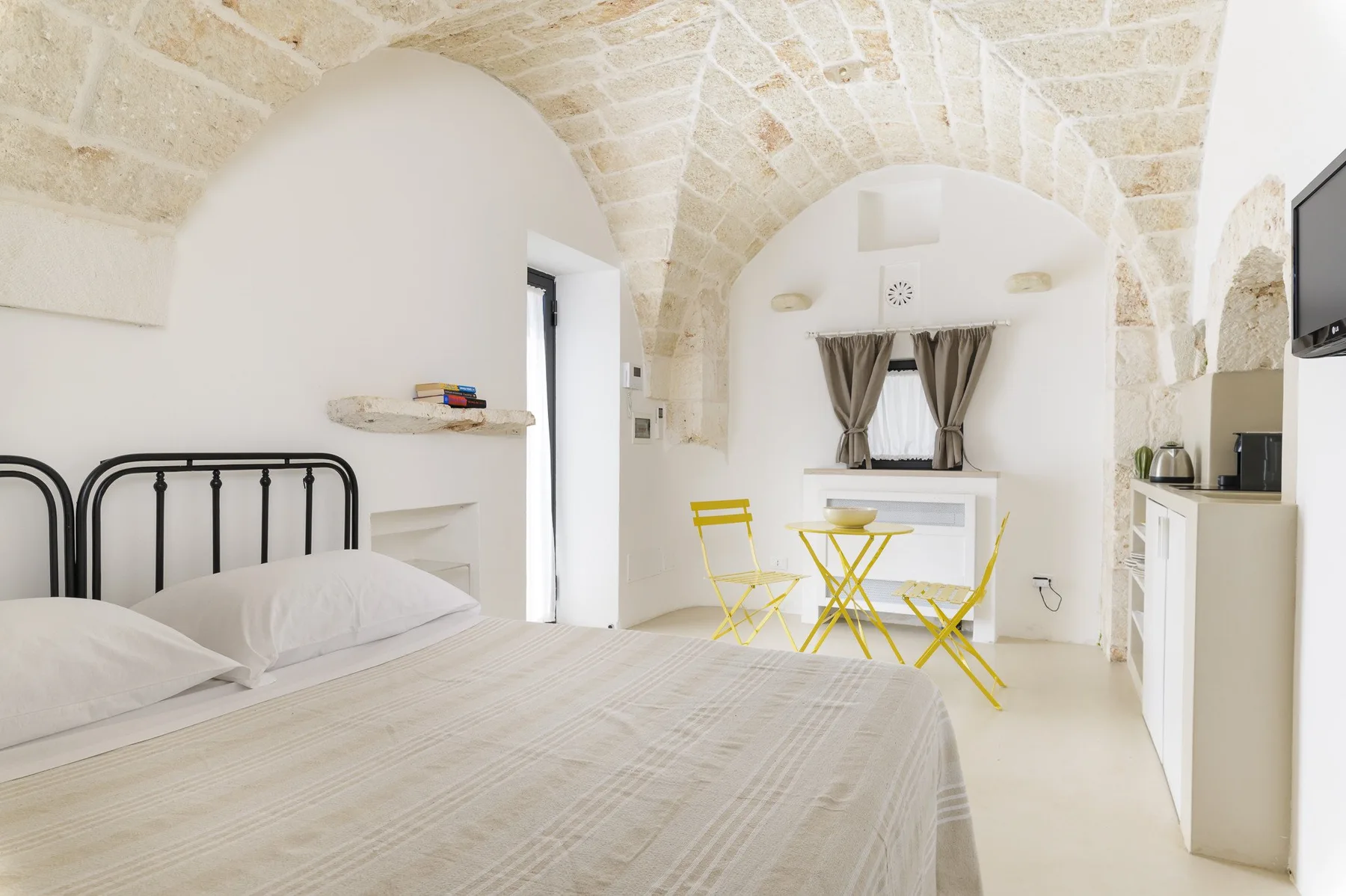 A bright bedroom with a bed beneath a pale stone vaulted ceiling.