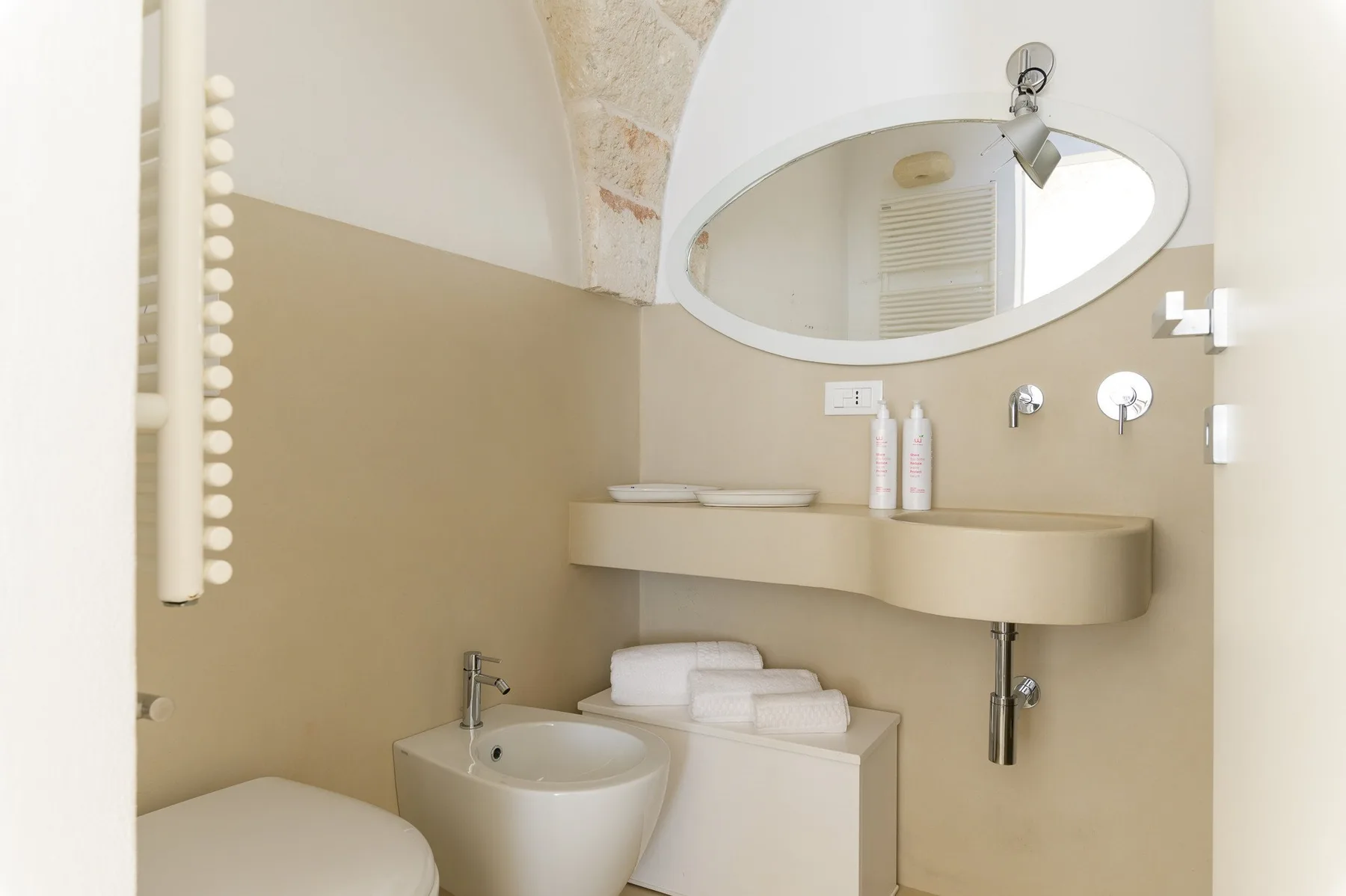 Un baño con lavabo redondeado, espejo de pared e inodoro.