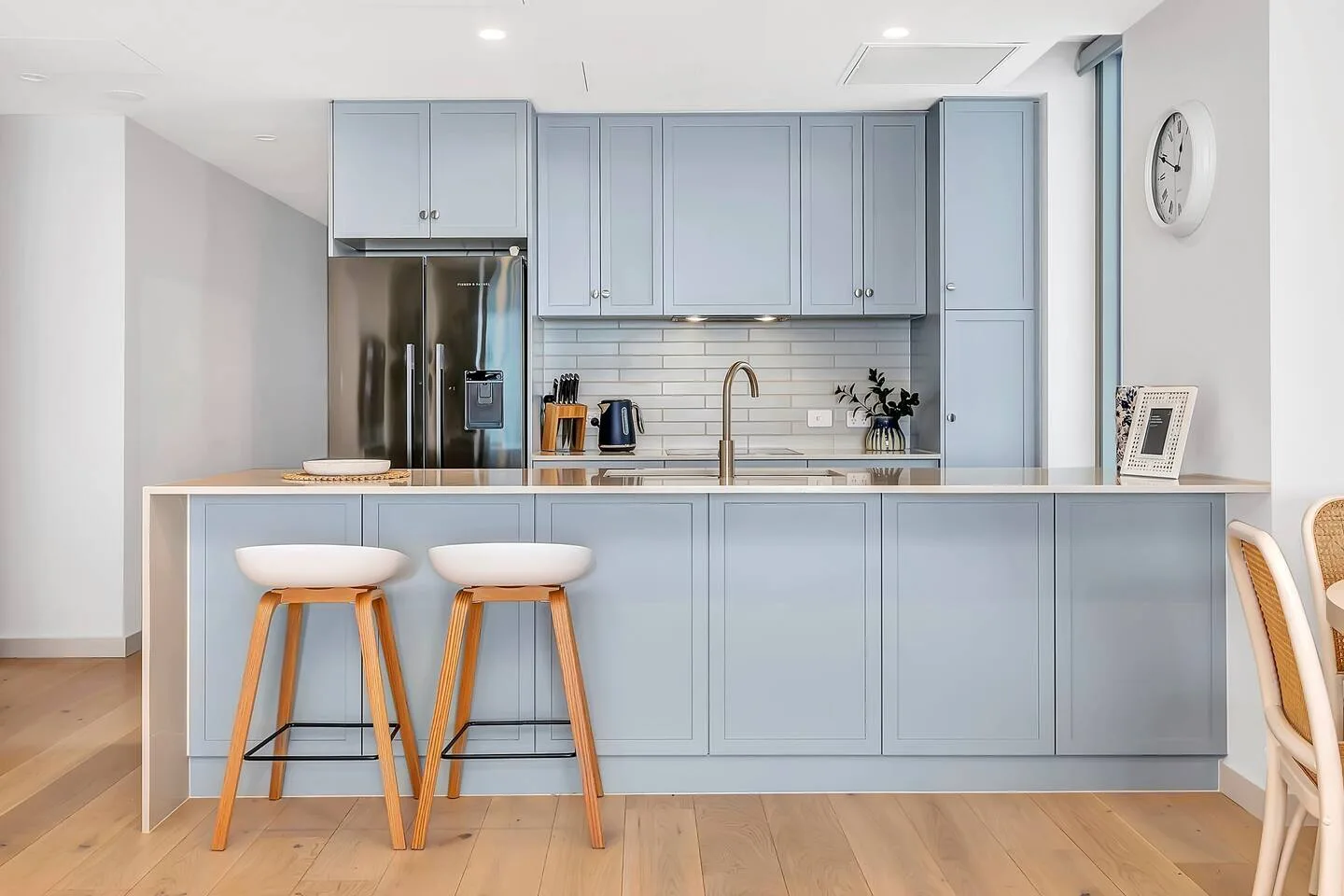 Una cocina luminosa con gabinetes azul claro, una encimera y taburetes.