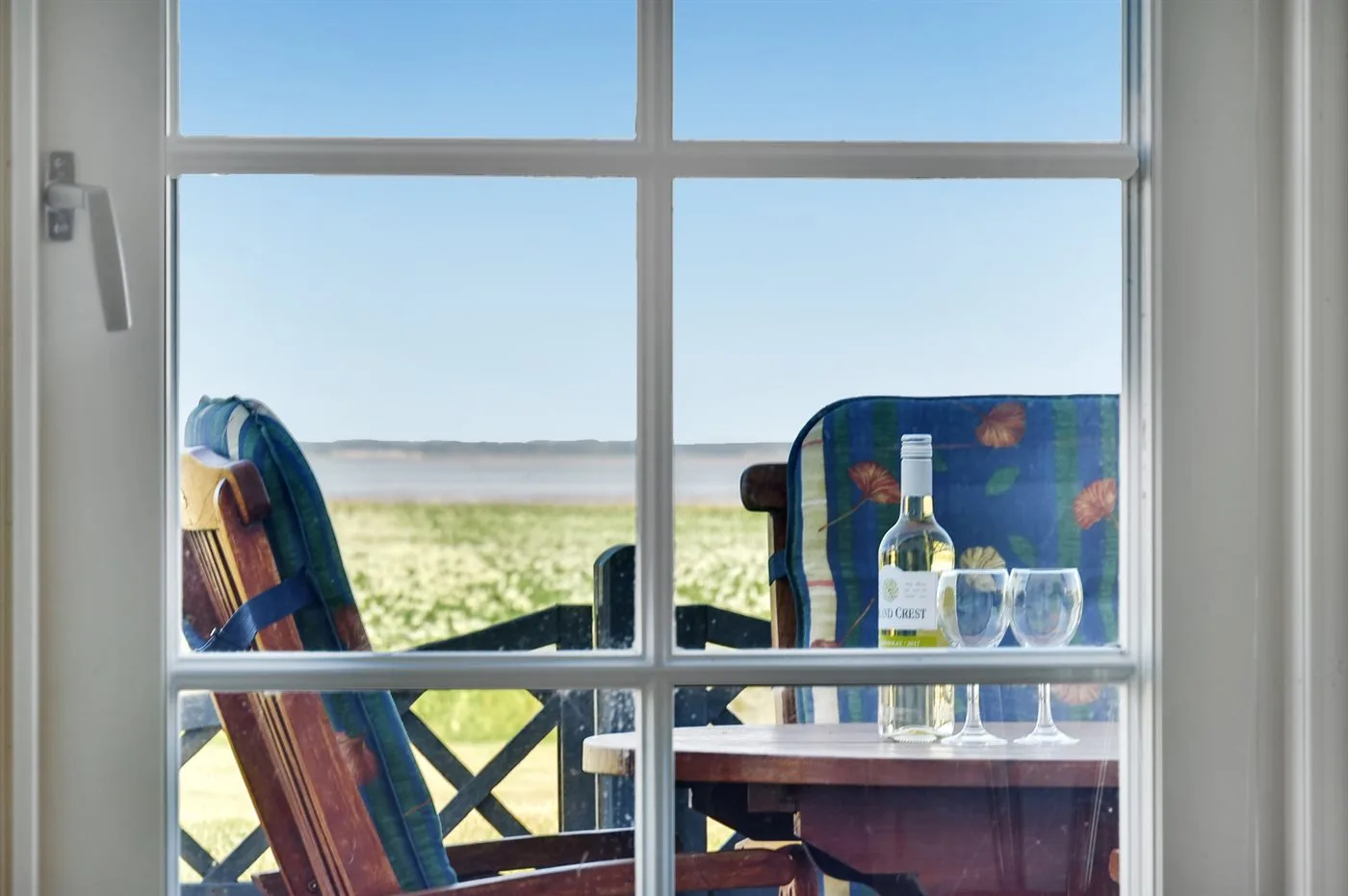 A window overlooks open fields beside a balcony seating area with drinks.