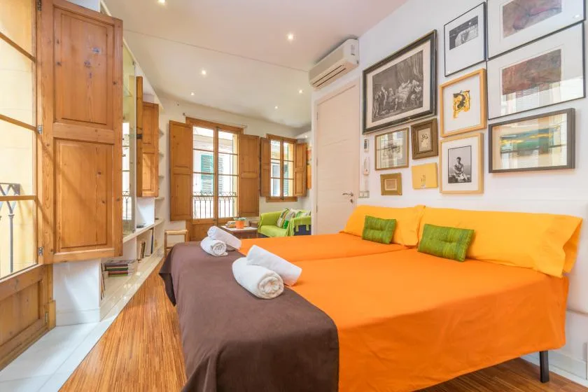 A bedroom with a bright orange bedspread and framed pictures on the wall.