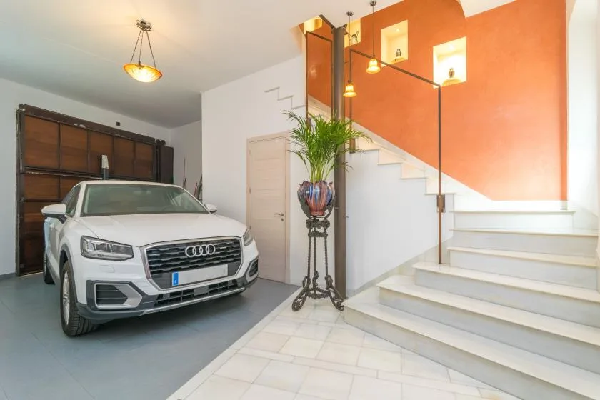 An indoor garage and staircase share a bright entry space with a parked car.