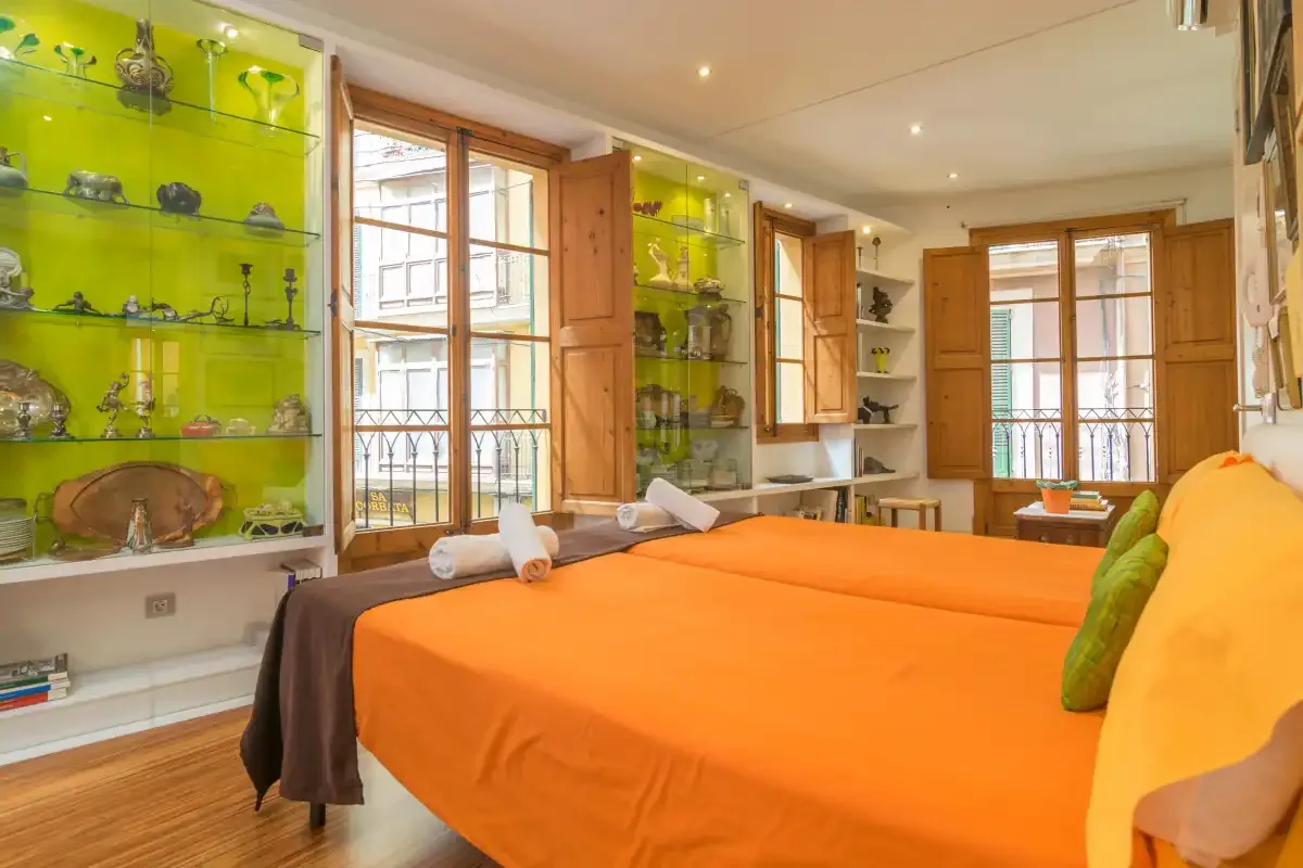 A bedroom with orange bedding and display shelves along the wall.