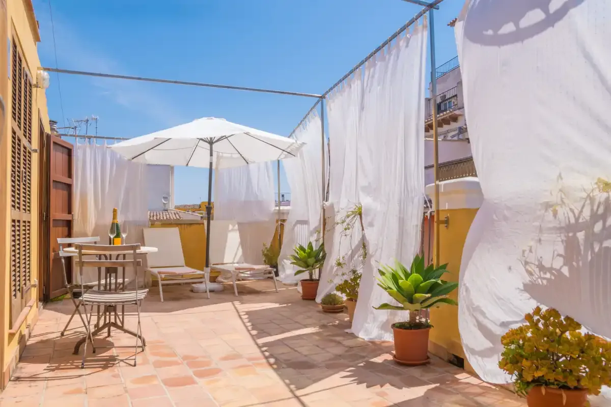 A sunny terrace with a patio umbrella, outdoor seating, and potted plants.