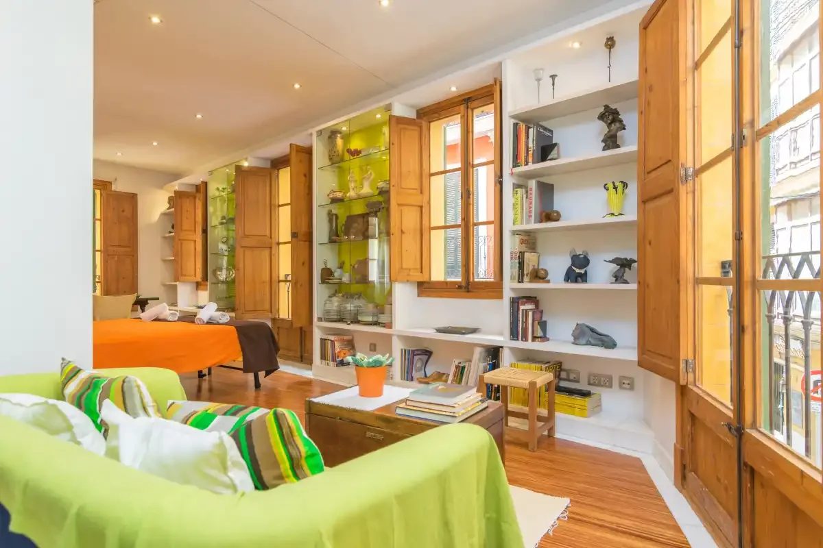 A bright living room with seating, built-in shelves, and tall windows.