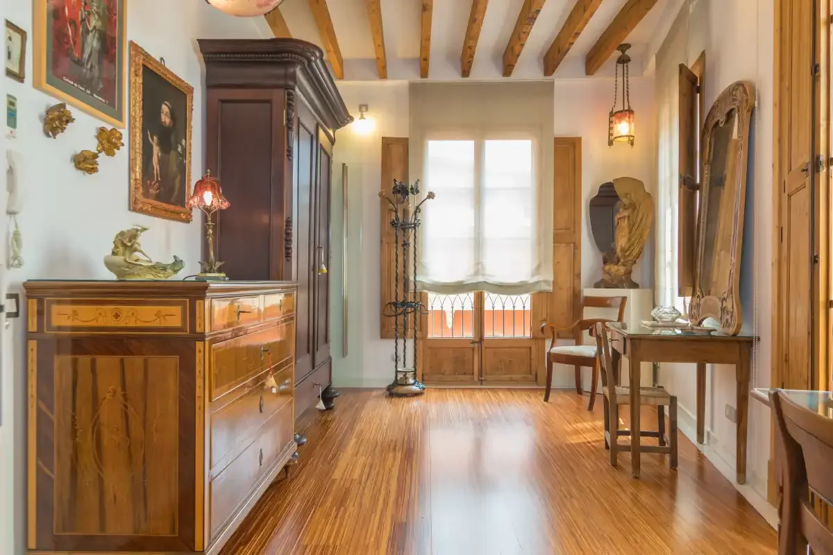 A furnished room with wooden furniture, exposed ceiling beams, and a bright window.