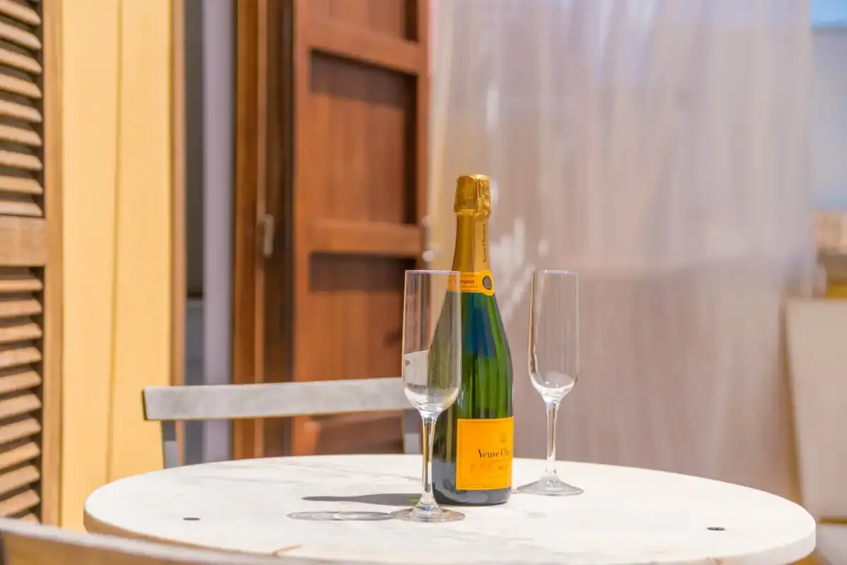 A bottle and two glasses sit on a small round table beside a wooden door.