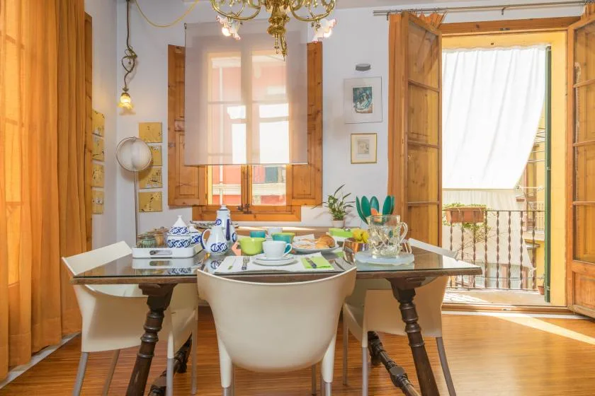 A dining area with a set table beside open wooden doors and a curtained window.