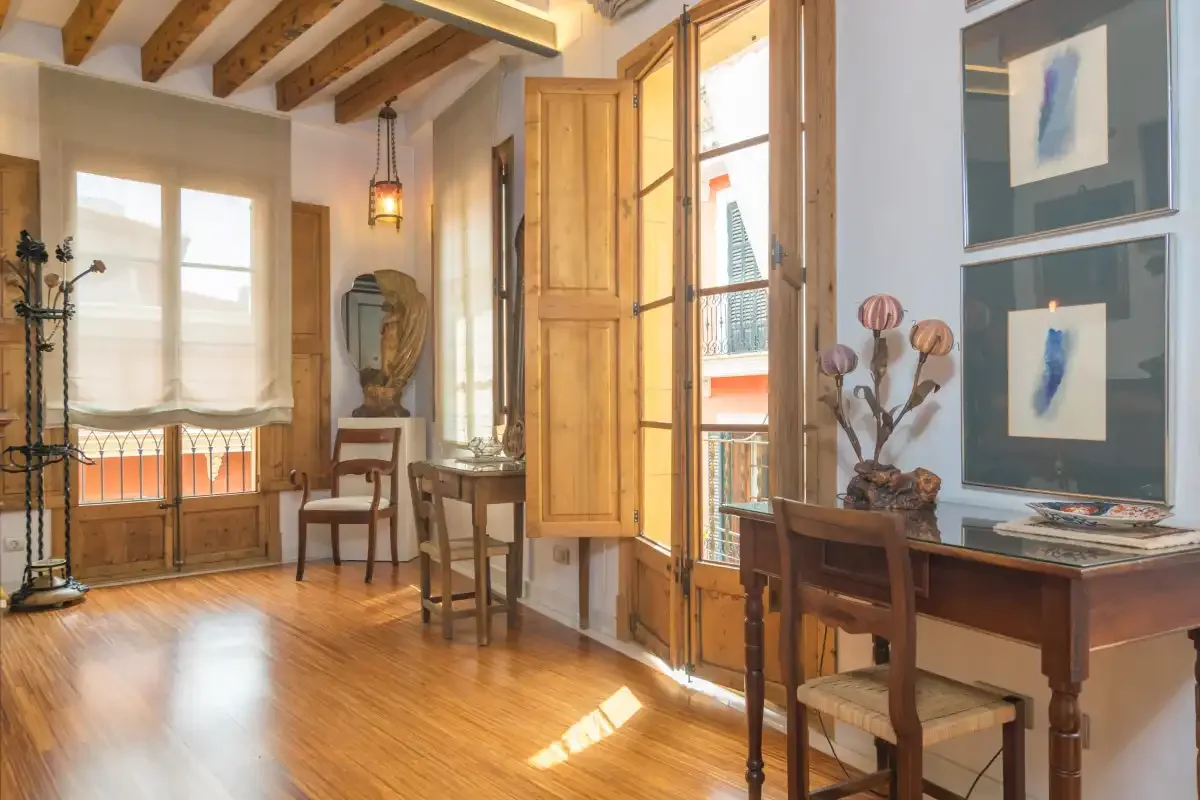 A bright interior room with a wooden table, chairs, and tall windows.