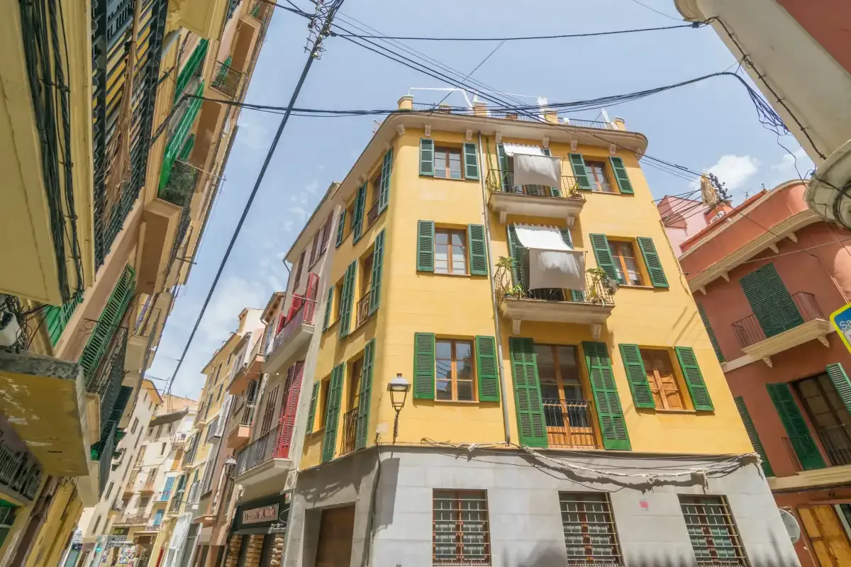 A yellow apartment building with green shutters on a narrow city street.