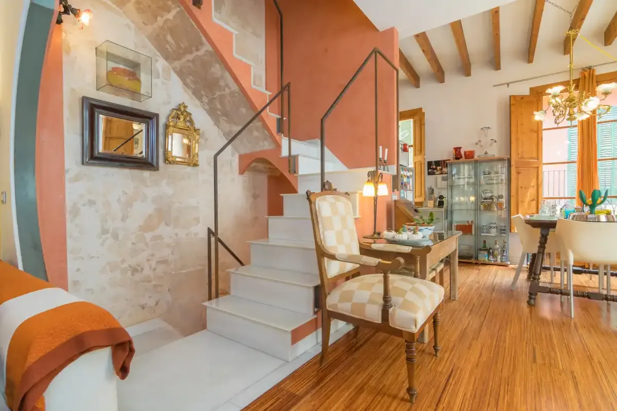 A bright living and dining area with a staircase and exposed ceiling beams.