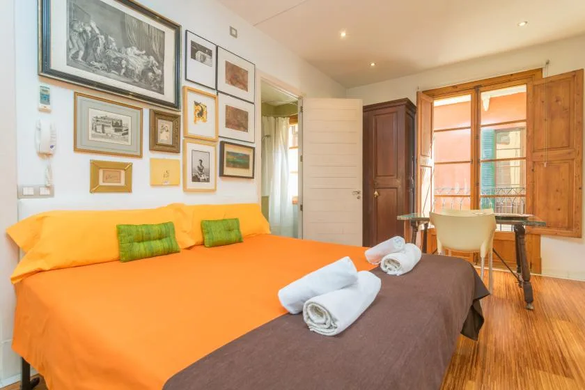 A bedroom with a bright orange bed, framed pictures, and wooden window shutters.