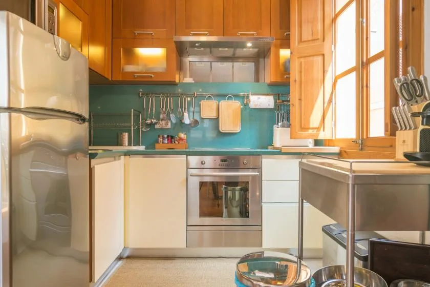 A bright kitchen with wooden cabinets, a turquoise backsplash, and stainless-steel appliances.