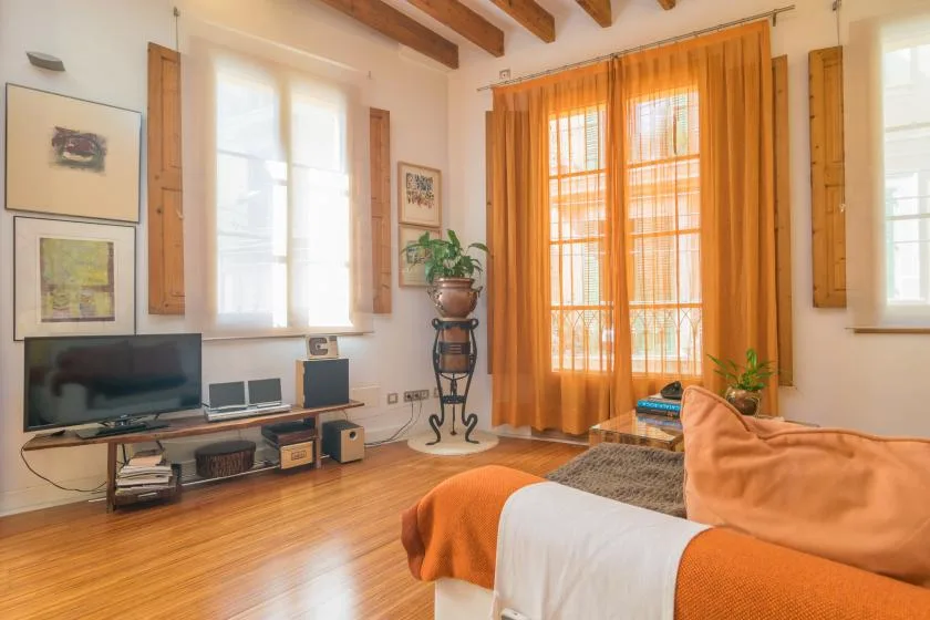 Una sala de estar con asientos, un televisor y cortinas naranjas.