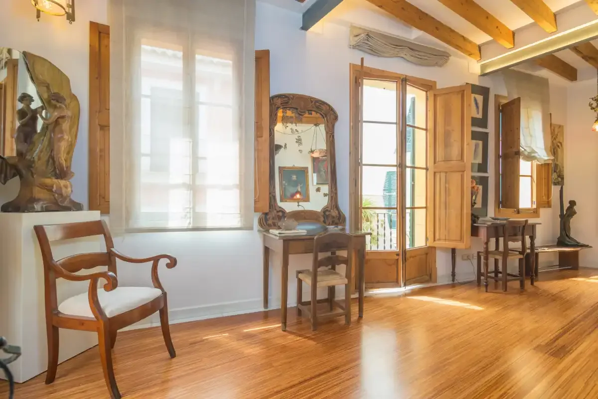 A bright room with wooden floors, tall windows, and a small table beneath a mirror.