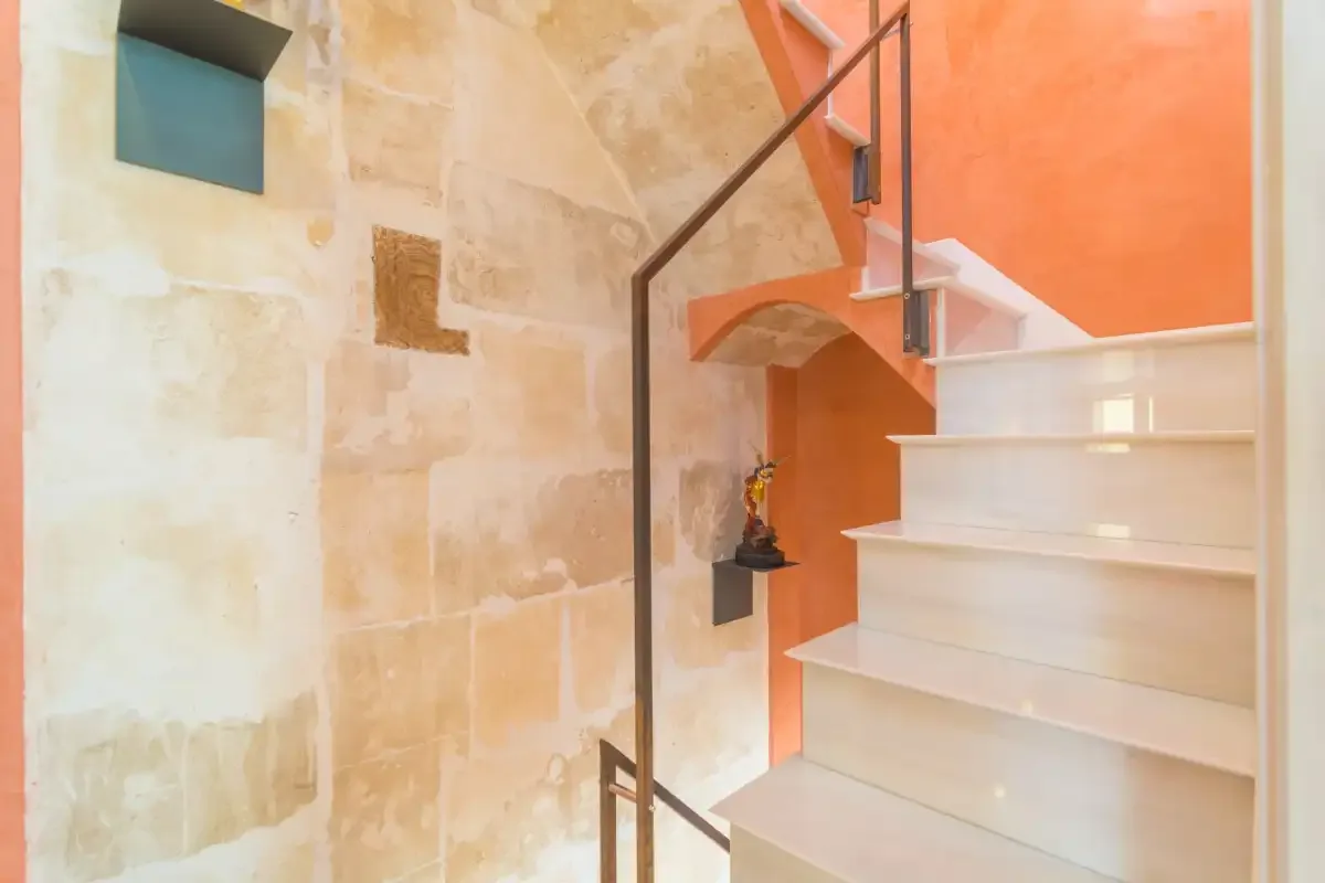 A staircase with white steps and a dark railing beside a stone wall.