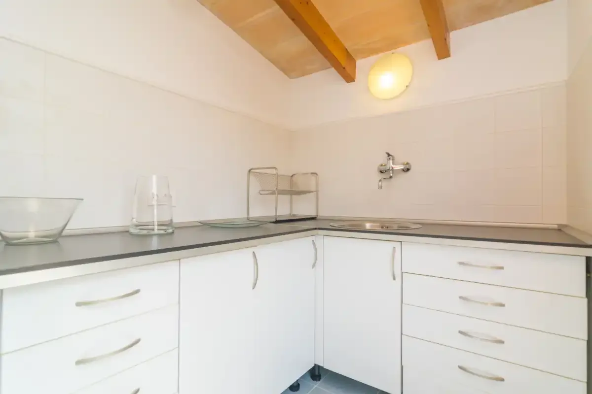A bright kitchen with white cabinets, a countertop, and exposed ceiling beams.