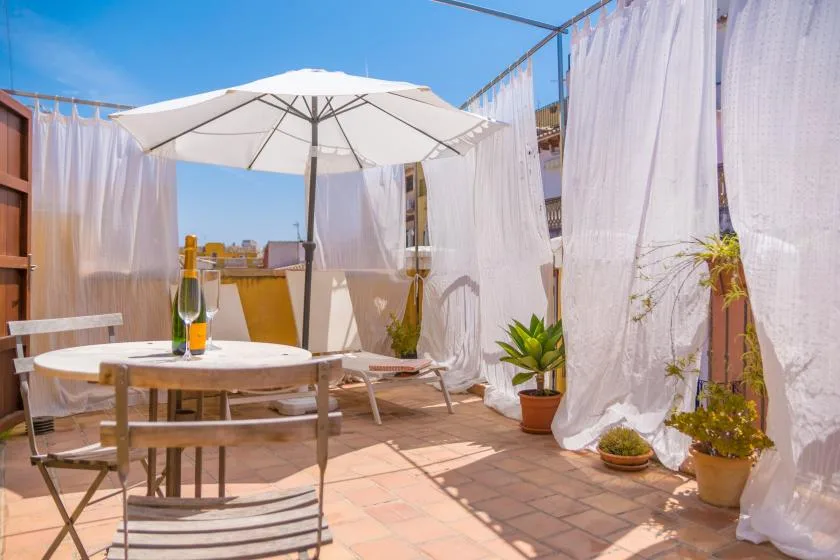 A sunlit terrace has a round table beneath a large white umbrella.