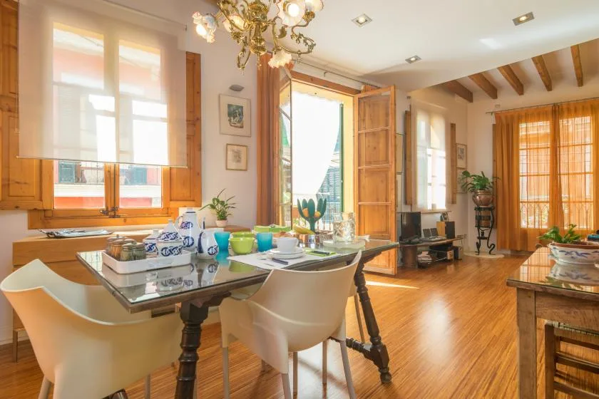 A bright dining area with a set table, large windows, and an open wooden door.