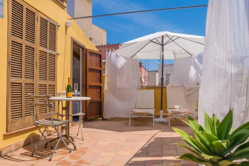 A sunny outdoor patio with a white umbrella, seating, and potted plants.