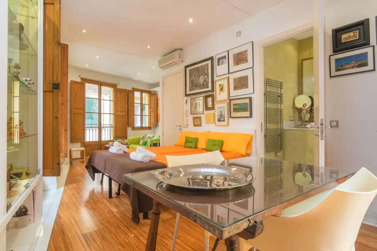 A bedroom with an orange bed, framed pictures, and a glass-topped table.