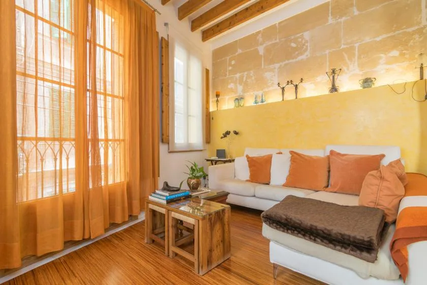 A bright living room with seating, orange curtains, and exposed ceiling beams.