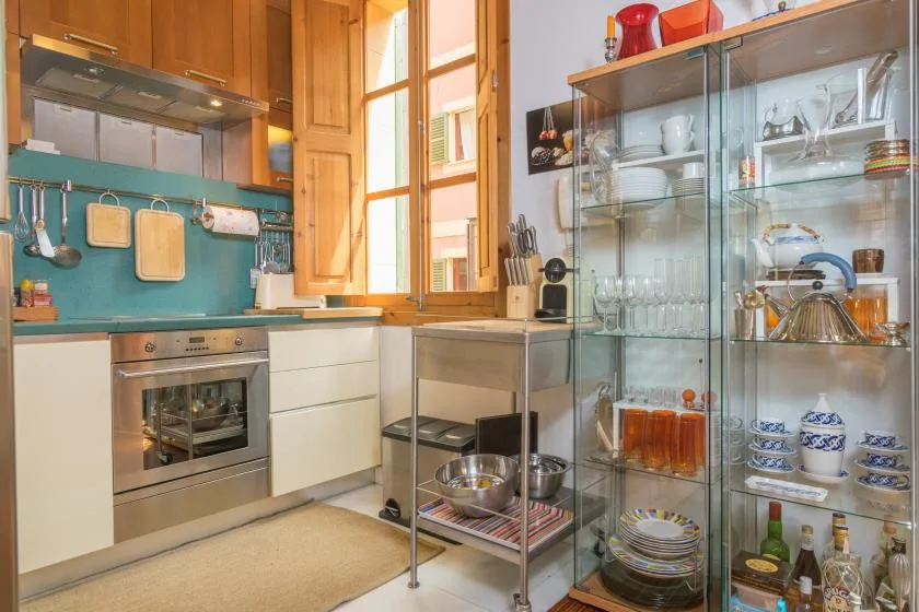 A kitchen with wooden cabinetry, a teal backsplash, and glass-fronted dish storage.